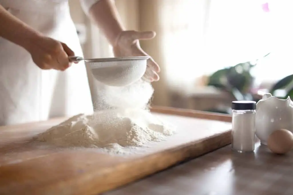 hands sifting flour onto a wood board