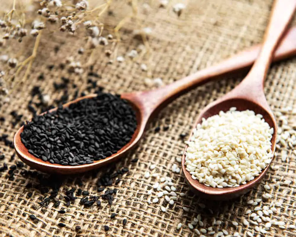 Black and white sesame seeds in wooden spoons on burlap surface