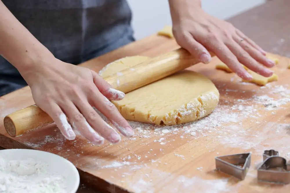 Female hands rolling out cookie dough with a wooden rolling pin