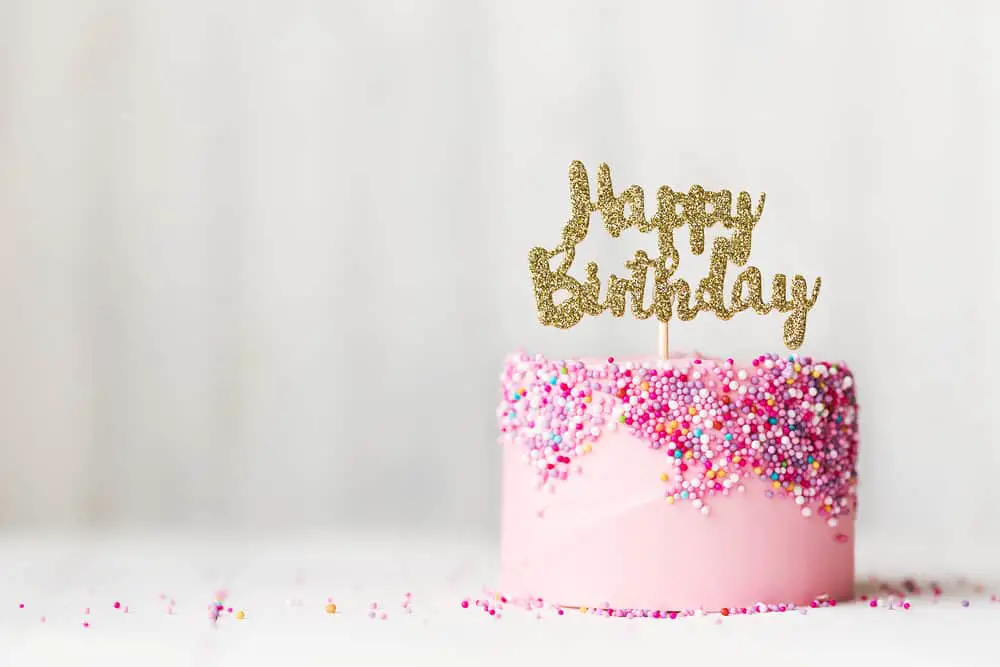 "Happy Birthday" cake topper on pink cake covered in sprinkles