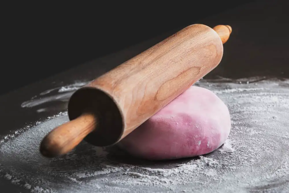 Rolling pin on pink fondant sitting on powdered surface