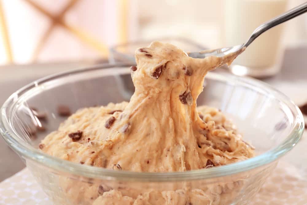 Spoon lifting raw chocolate chip cookie dough from glass bowl