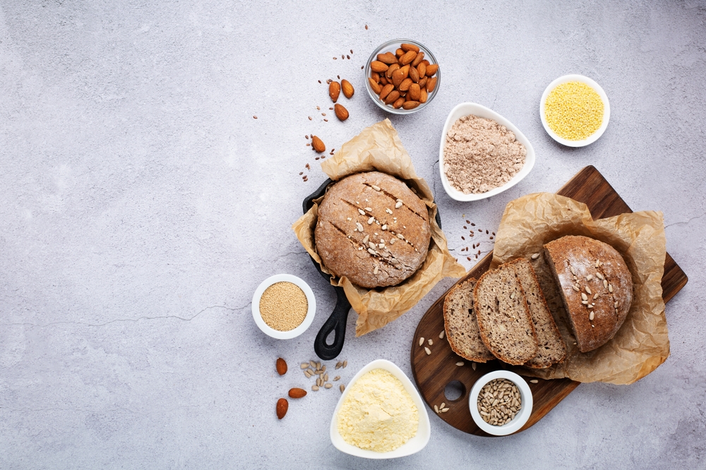 Gluten-free homemade vegan bread on cutting board with nuts in bowls alongside