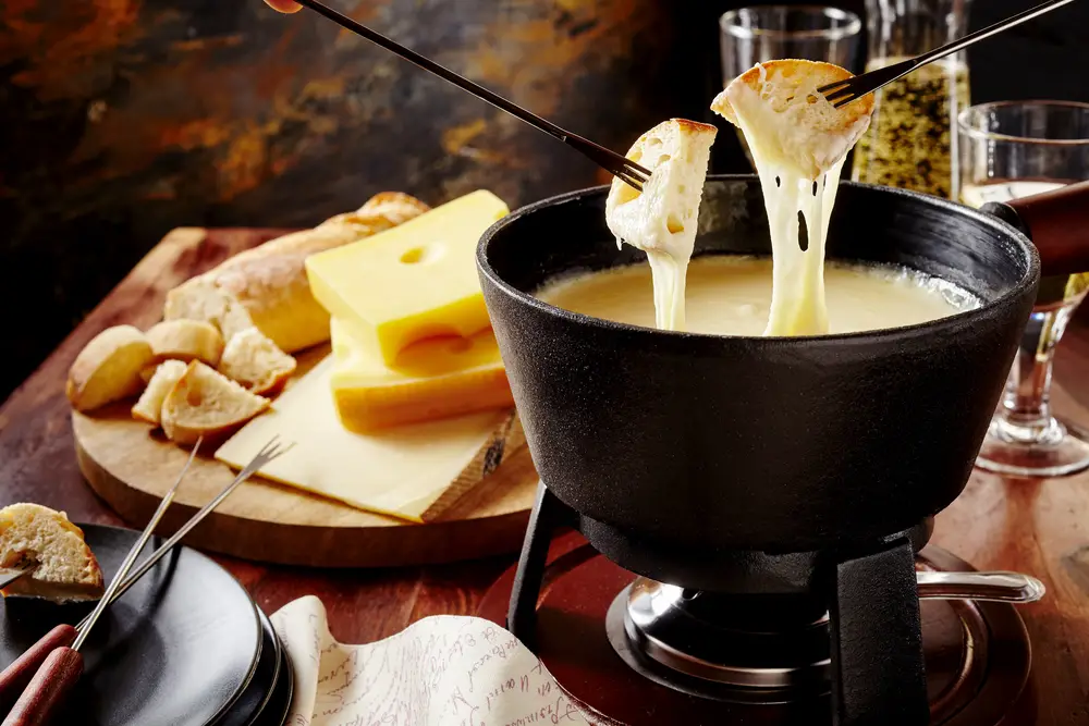 Gourmet Swiss cheese fondue dipping bread in melted cheese pot