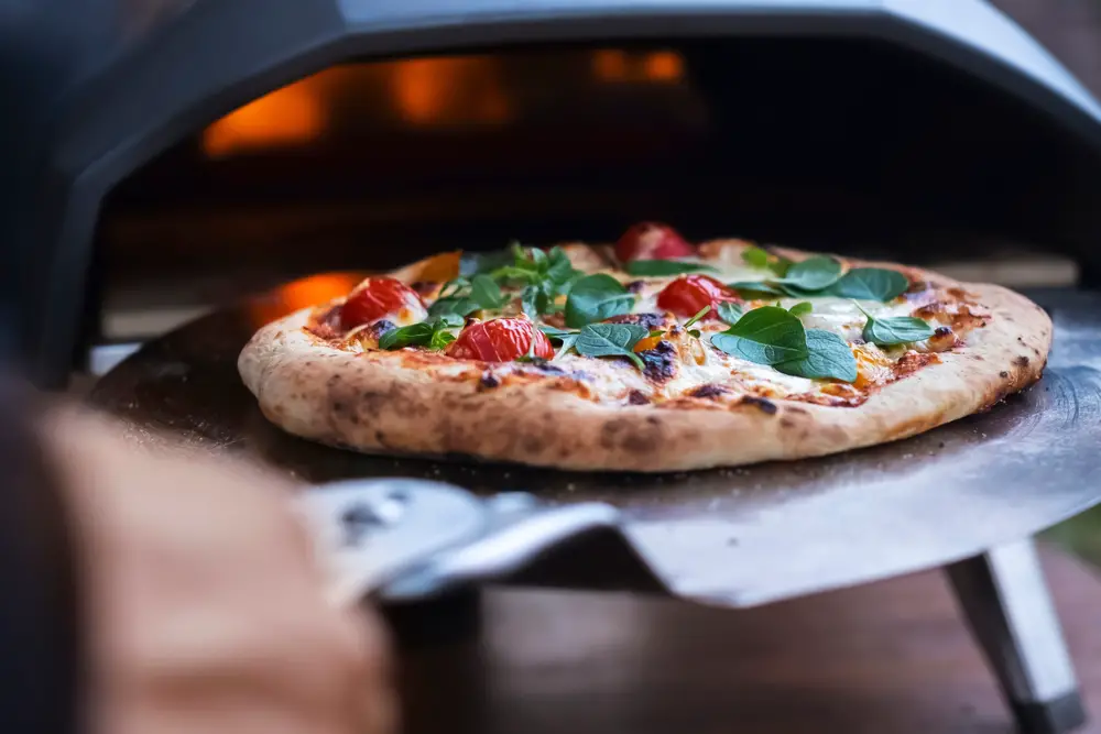 Homemade pizza coming out of pizza oven with fresh toppings