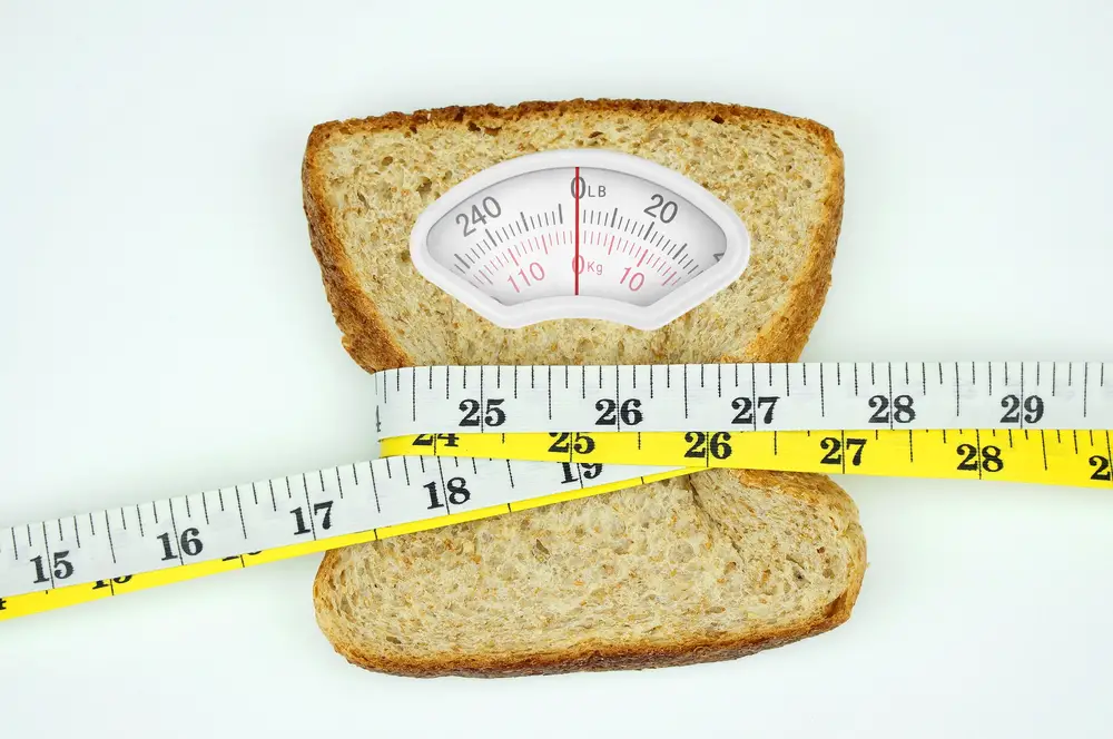 Slice of whole wheat bread with weight scale and tape measure on it