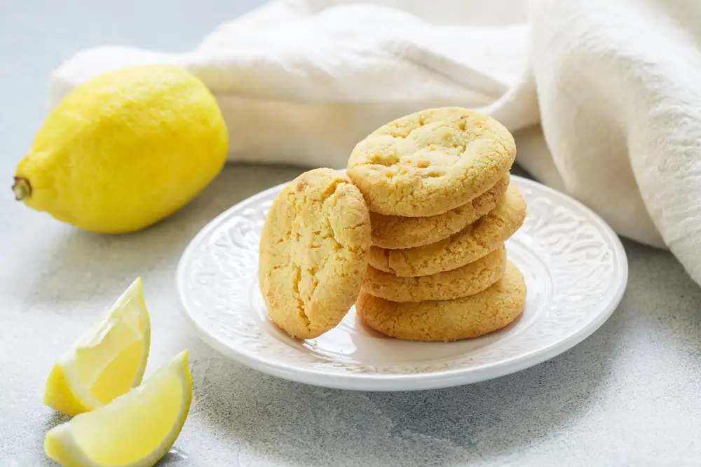 Stack of homemade lemon cookies on white plate with lemons beside