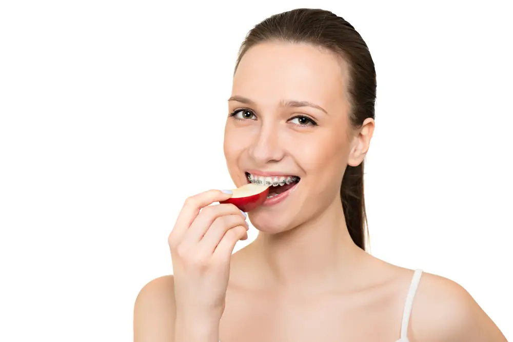 Young woman with braces eating apple slice