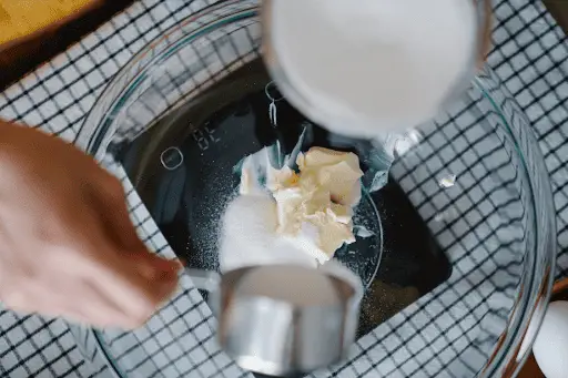 Baker pouring Wondra flour and sugar into glass bowl with butter