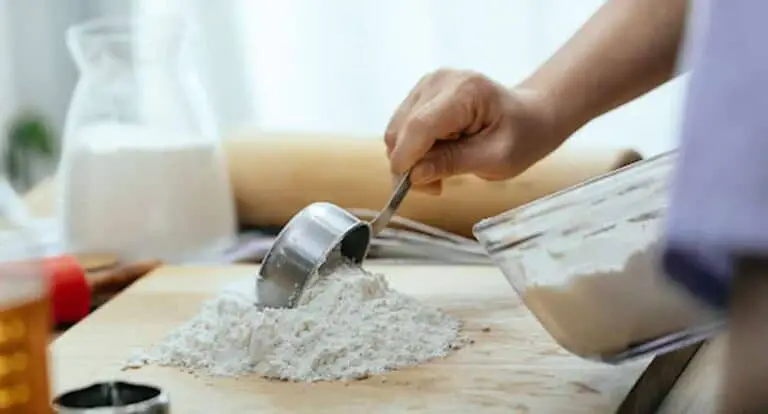 Baker-scooping-flour-from-bowl-onto-board-with-measuring-cup