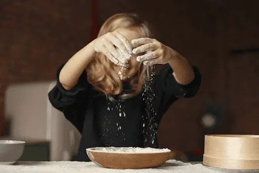 Girl letting flour fall through her fingers into wooden bowl