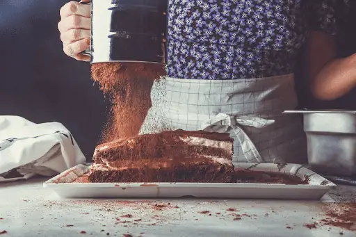 Woman shaking cocoa onto cake with flour sifter